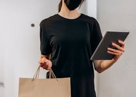A woman in casual attire delivers packages while checking her tablet indoors, embodying the modern delivery lifestyle.
